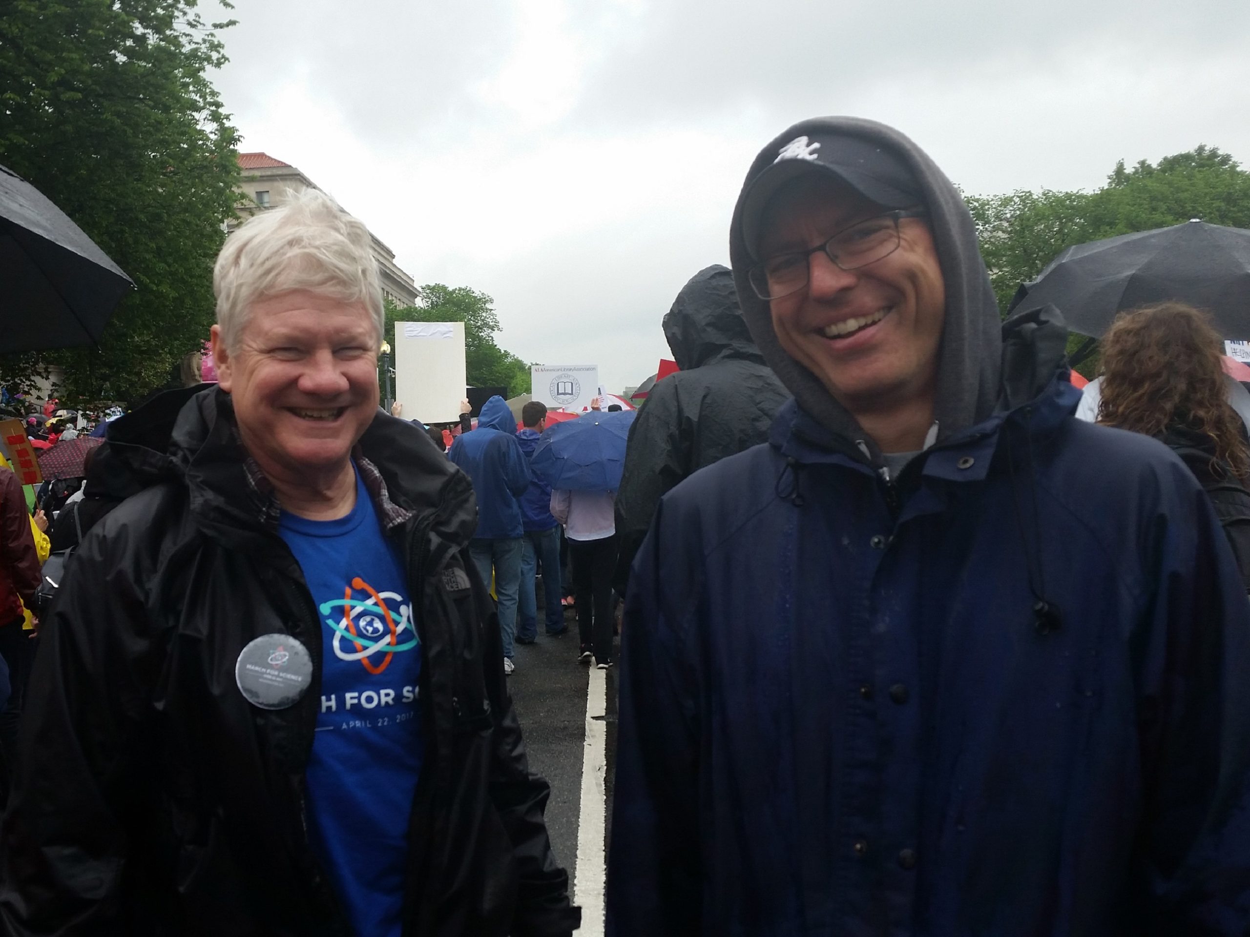 Two men smiling outside in the rain.